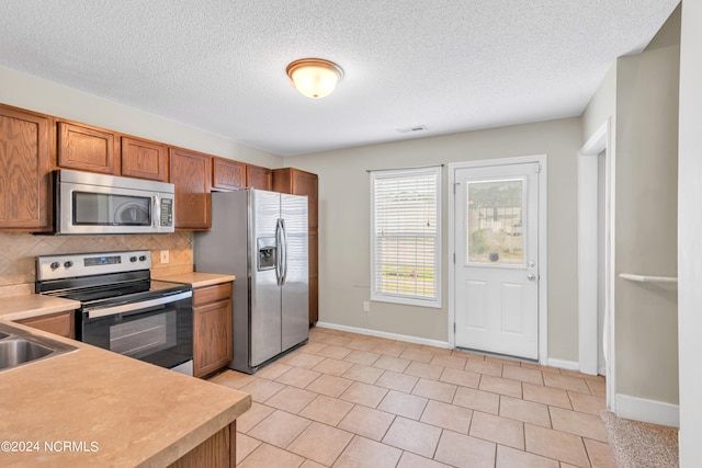 kitchen featuring a textured ceiling, backsplash, stainless steel appliances, and light tile patterned flooring