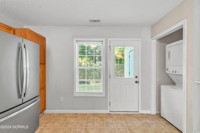 doorway to outside with a textured ceiling and stacked washer and clothes dryer