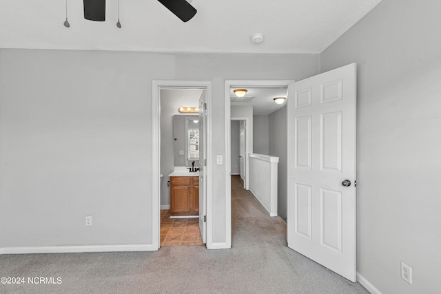 unfurnished bedroom with ceiling fan, ensuite bathroom, and light carpet