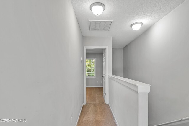 hall featuring a textured ceiling and light colored carpet