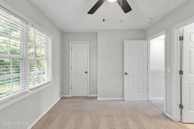 unfurnished bedroom with ceiling fan, light colored carpet, and a textured ceiling