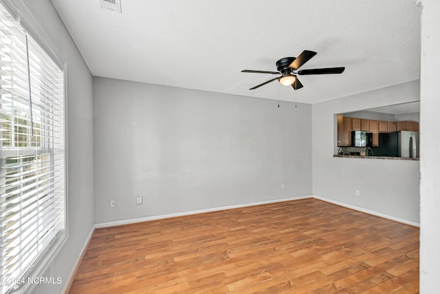 unfurnished living room featuring a textured ceiling, a healthy amount of sunlight, ceiling fan, and light hardwood / wood-style floors