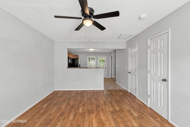 unfurnished living room featuring a textured ceiling, baseboards, and wood finished floors