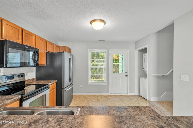 kitchen featuring appliances with stainless steel finishes, stacked washer and clothes dryer, and a textured ceiling