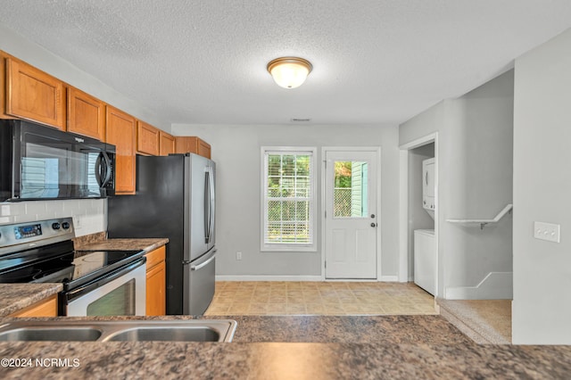 kitchen featuring stacked washer and dryer, tasteful backsplash, brown cabinets, stainless steel appliances, and a textured ceiling