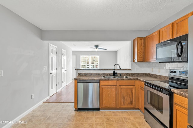 kitchen featuring dark countertops, brown cabinets, a peninsula, stainless steel appliances, and a sink