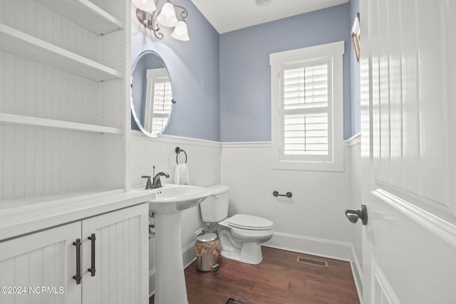 half bath with wainscoting, toilet, wood finished floors, and visible vents