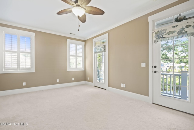 empty room featuring light colored carpet, ornamental molding, baseboards, a ceiling fan, and visible vents