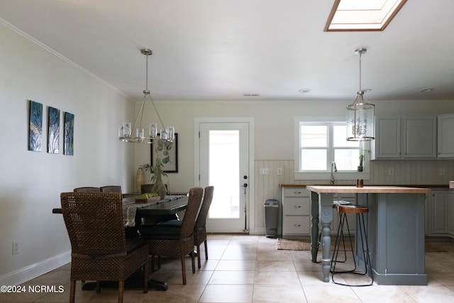 tiled dining room featuring sink, a skylight, ornamental molding, and a notable chandelier