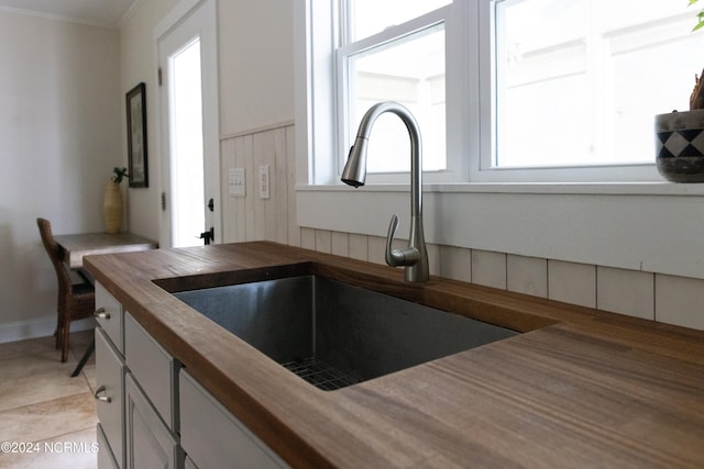 kitchen with light tile patterned floors, butcher block countertops, crown molding, and sink