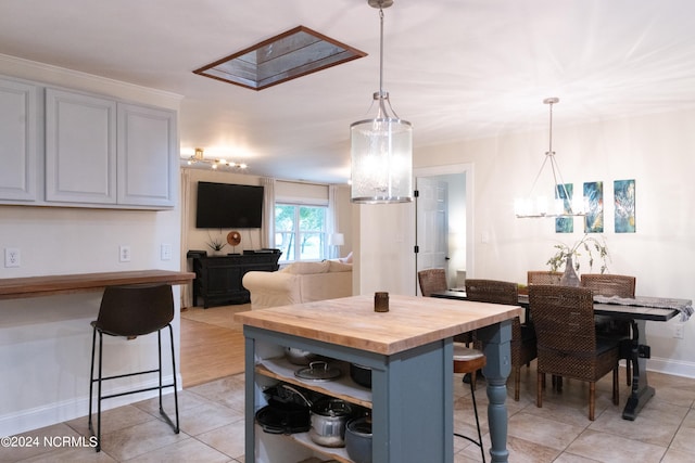 kitchen with wood counters, a kitchen breakfast bar, decorative light fixtures, a center island, and light tile patterned flooring