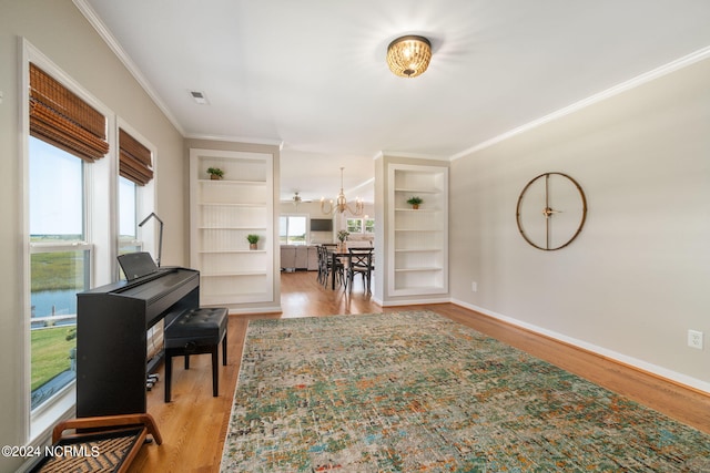 miscellaneous room featuring a water view, ornamental molding, light hardwood / wood-style floors, built in shelves, and a chandelier