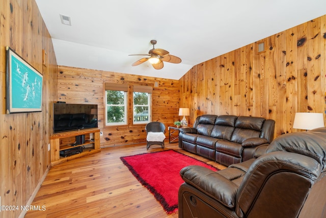 living room with ceiling fan, wooden walls, light wood-type flooring, and vaulted ceiling