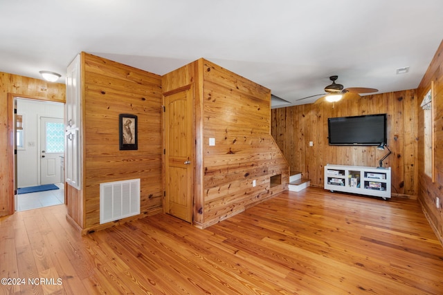 unfurnished living room with light wood-type flooring, wood walls, and ceiling fan