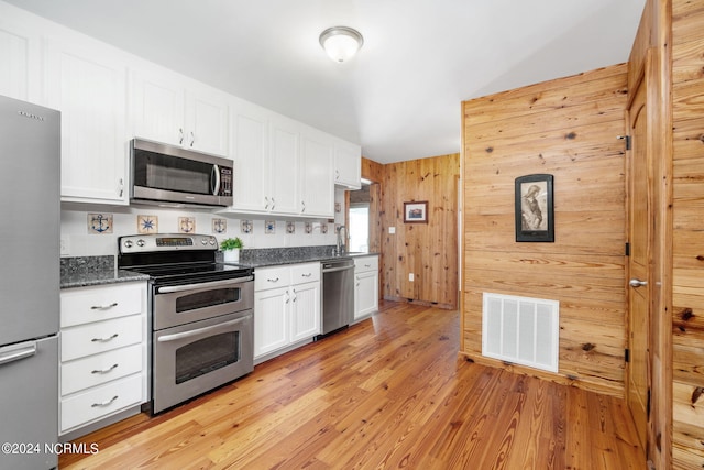 kitchen featuring wooden walls, light hardwood / wood-style flooring, stainless steel appliances, and white cabinets