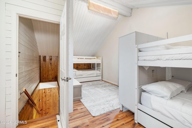 bedroom with light hardwood / wood-style flooring, wood walls, and lofted ceiling with beams