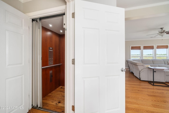 corridor with elevator, ornamental molding, and light wood-type flooring