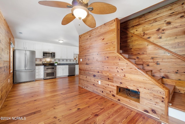 kitchen with stainless steel appliances, white cabinetry, wooden walls, and light hardwood / wood-style flooring