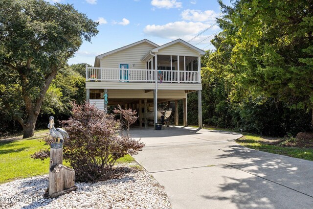 raised beach house with concrete driveway, a carport, and a sunroom