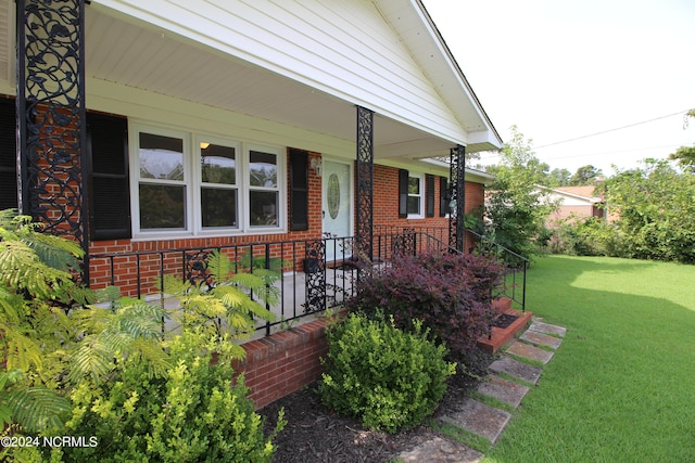 doorway to property with covered porch and a yard