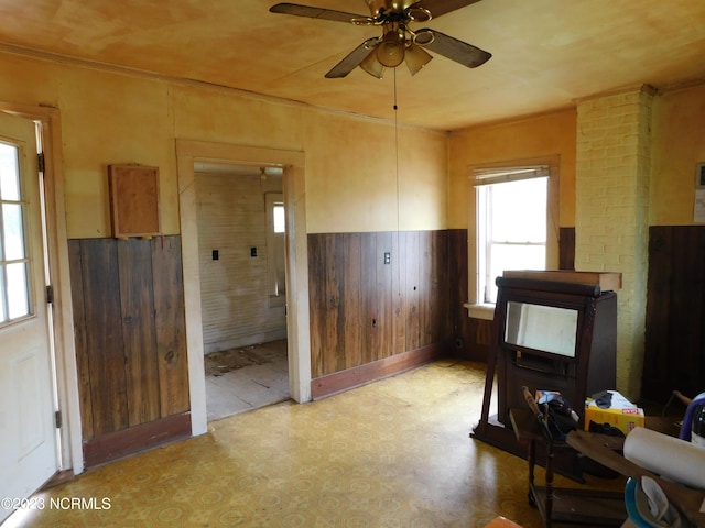 interior space with wood walls, wainscoting, a wood stove, and a ceiling fan