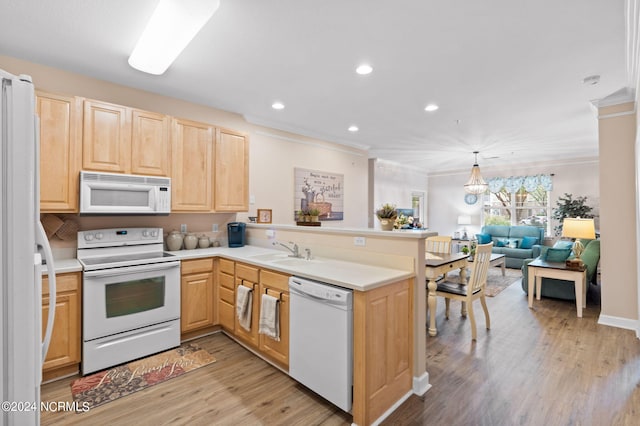 kitchen with a sink, a peninsula, white appliances, and light brown cabinets