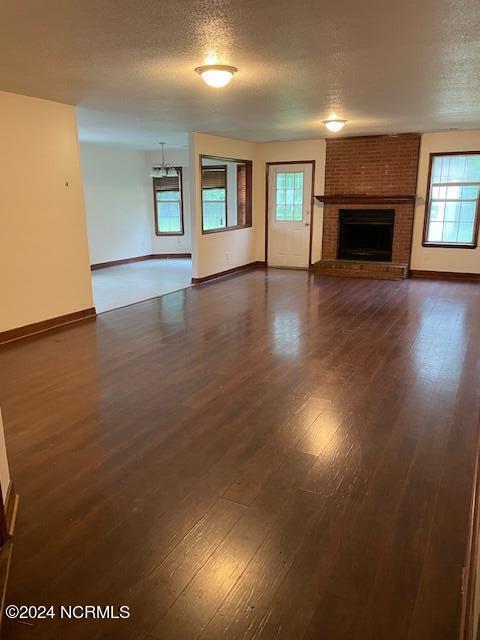 unfurnished living room with a textured ceiling, dark wood-type flooring, a fireplace, and baseboards