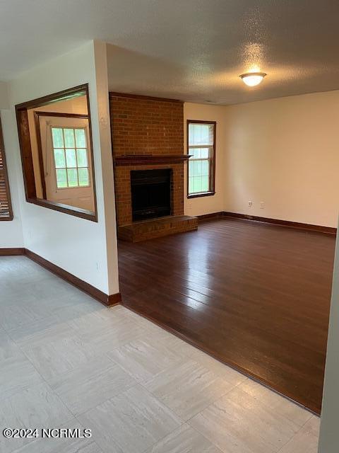 unfurnished living room with light hardwood / wood-style floors, brick wall, a textured ceiling, and a brick fireplace