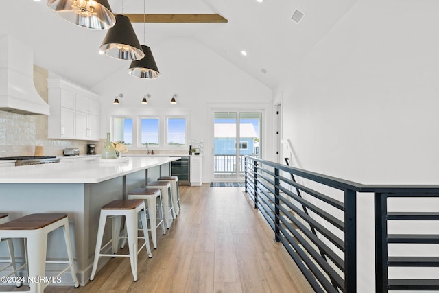 kitchen with tasteful backsplash, a kitchen bar, white cabinetry, wine cooler, and high vaulted ceiling