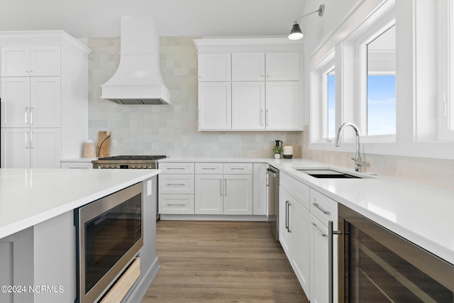 kitchen featuring appliances with stainless steel finishes, white cabinetry, light hardwood / wood-style floors, wine cooler, and premium range hood