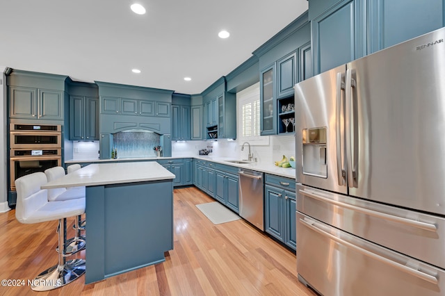 kitchen with tasteful backsplash, a kitchen island, appliances with stainless steel finishes, sink, and light hardwood / wood-style flooring