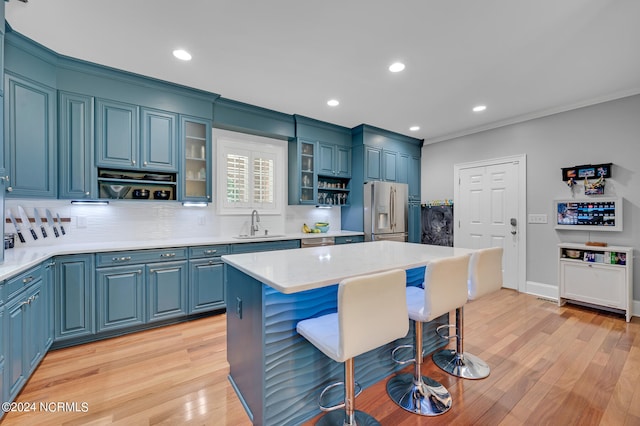 kitchen with a kitchen island, blue cabinetry, stainless steel fridge with ice dispenser, a breakfast bar area, and light hardwood / wood-style flooring