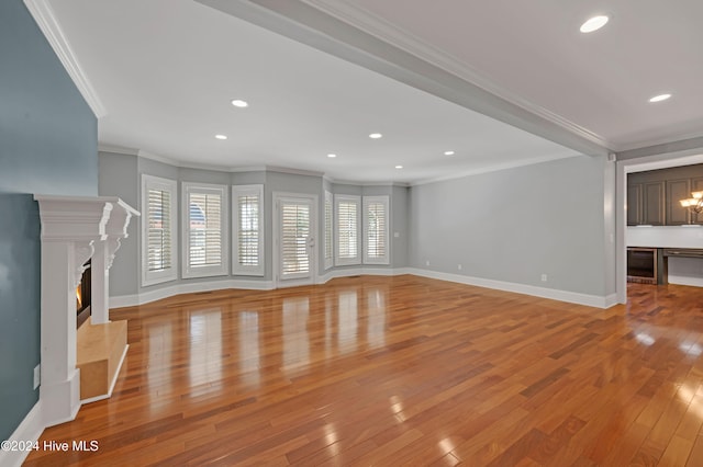 unfurnished living room featuring beverage cooler, a premium fireplace, a chandelier, ornamental molding, and light wood-type flooring