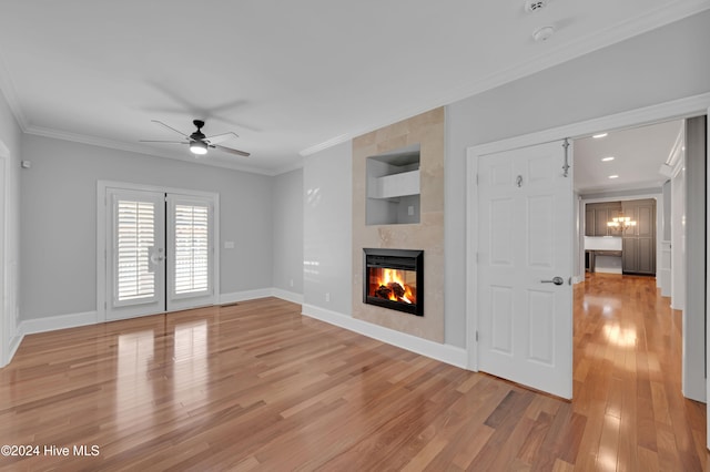 unfurnished living room featuring a tiled fireplace, ceiling fan with notable chandelier, light hardwood / wood-style floors, and crown molding