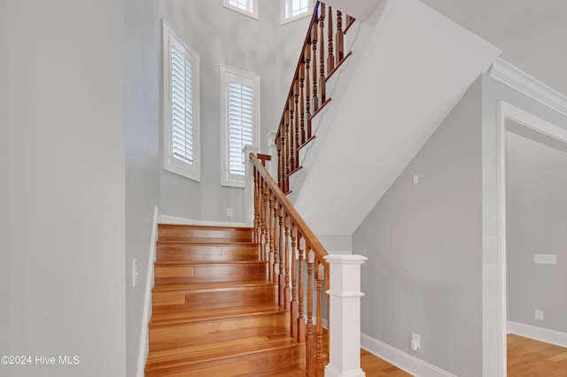 staircase featuring a wealth of natural light, wood-type flooring, and crown molding