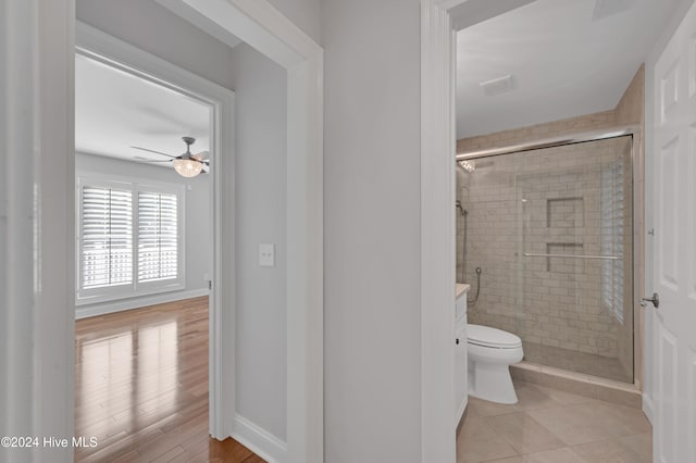 bathroom featuring hardwood / wood-style flooring, toilet, a shower with door, and ceiling fan