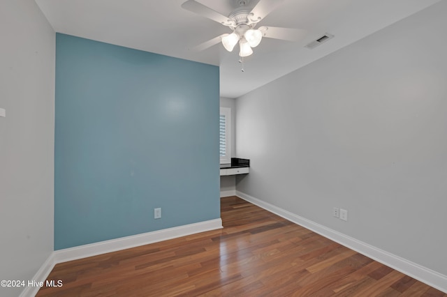 spare room with dark wood-type flooring, built in desk, and ceiling fan