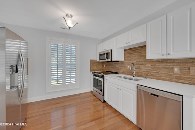 kitchen with stainless steel appliances, white cabinetry, sink, and light hardwood / wood-style flooring