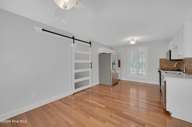 kitchen with stainless steel appliances, a barn door, sink, backsplash, and white cabinetry