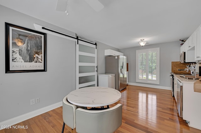 dining space featuring a barn door, ceiling fan, and light wood-type flooring