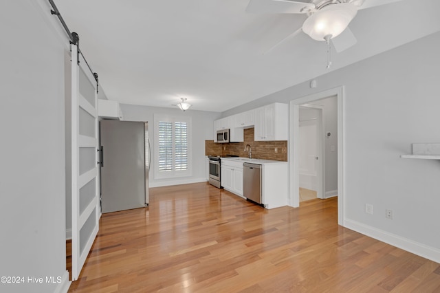 kitchen featuring white cabinets, appliances with stainless steel finishes, a barn door, and light hardwood / wood-style flooring