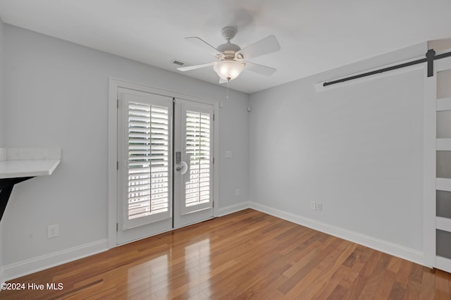 empty room featuring hardwood / wood-style floors, ceiling fan, and a barn door