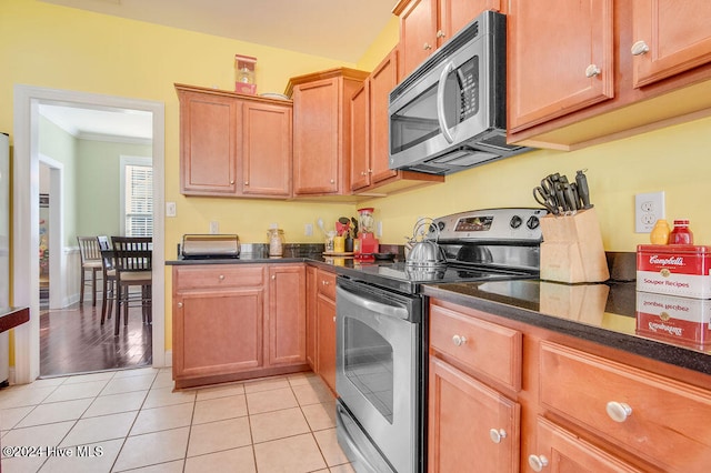 kitchen featuring dark stone countertops, light tile patterned floors, stainless steel appliances, and ornamental molding