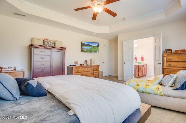 bedroom with ceiling fan, a raised ceiling, ornamental molding, and ensuite bath