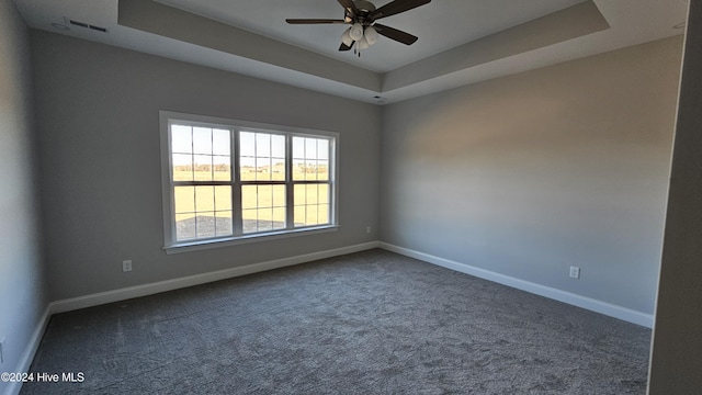 carpeted empty room with a ceiling fan, a tray ceiling, visible vents, and baseboards