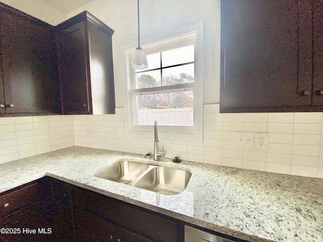 kitchen with hanging light fixtures, sink, dark brown cabinetry, and light stone counters