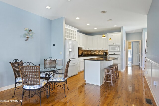 kitchen featuring hanging light fixtures, light hardwood / wood-style floors, white refrigerator with ice dispenser, sink, and an island with sink