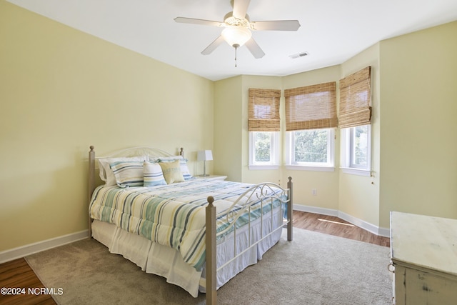 bedroom with a ceiling fan, visible vents, baseboards, and wood finished floors