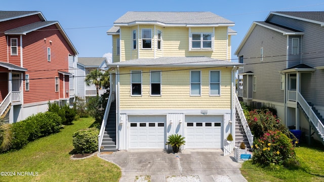 coastal inspired home featuring driveway, a garage, roof with shingles, stairs, and a front yard