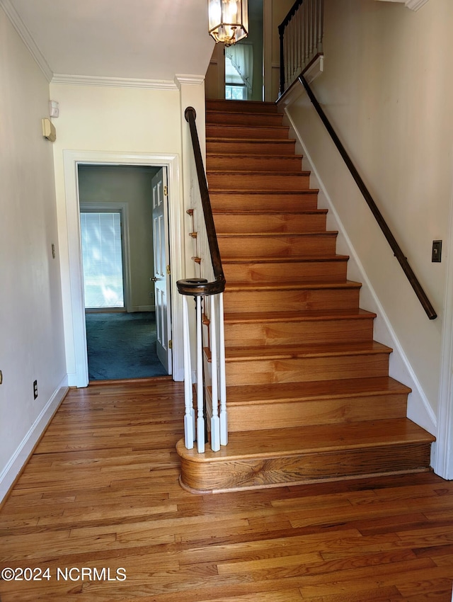 staircase with a wealth of natural light, crown molding, hardwood / wood-style floors, and a chandelier